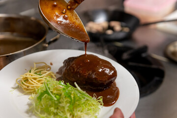 デミグラスソースをかけるハンバーグの調理シーン