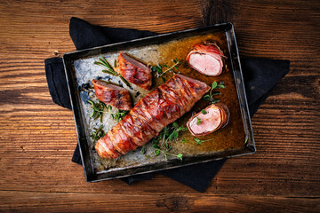 Pork fillet roast wrapped in prosciutto ham bacon with fresh herbs served as top view on roast tray 