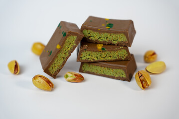 Pieces of pistachio-filled chocolate with scattered nuts on a clean white surface. Perfect for packaging mockups, dessert blogs, and advertising.