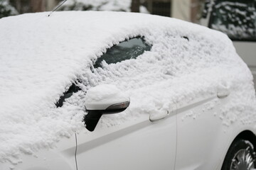 A close-up shot of a car heavily covered in fresh, wet snow on a winter day.