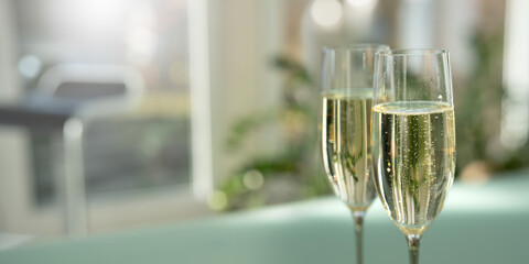Two elegant champagne glasses filled with sparkling wine and bright blurred bokeh lights in modern setting. Background for sophisticated celebrations. Close-up with space for text.