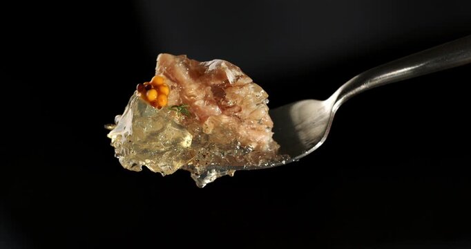 Aspic jellied meat with mustard on fork, close-up footage on dark background.