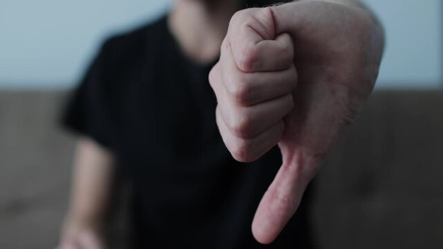 Unrecognizable young man showing a thumbs down gesture toward the camera. Negative feedback, disapproval, and bad review concept