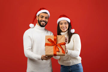 Two cheerful arab spouses are smiling while holding a beautifully wrapped Christmas gift box.