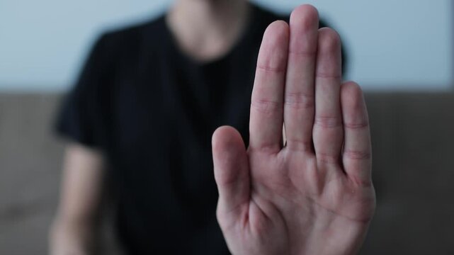 Close-up of a hand gesturing to stop, with a blurred figure in the background indicating denial, rejection, and disagreement