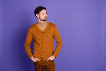 Young handsome brunet man in a warm cardigan and sweater stands against a violet background in...