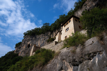 An impressive ancient stone dwelling precariously perched on a cliffside, stark against a blue sky, exhibiting historical significance and architectural grandeur in nature's embrace.