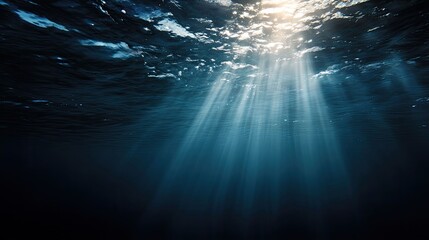 an underwater viewpoint from within the water column looking towards the surface. rays of light filter through the water to illuminate a portion of the scene below