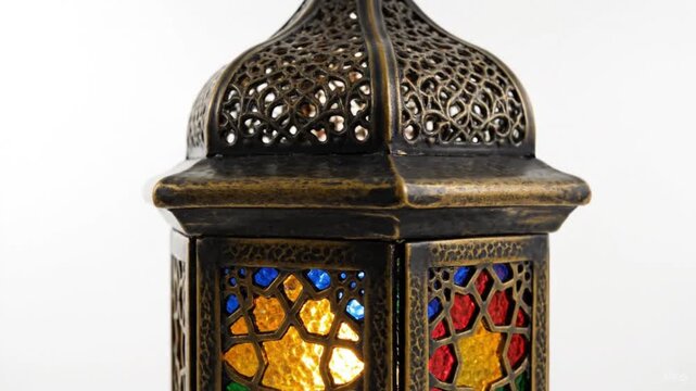 A beautifully detailed close-up shot captures an ornate metal lantern, exquisitely designed with intricate latticework and vibrant stained-glass panels. The glass sections glow warmly in shades of red