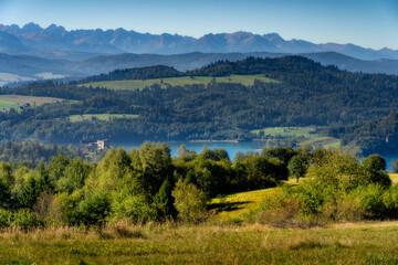 Scenic summer view of the tatra mountains and czorsztyn lake in poland, featuring lush green forests, rolling hills, and castle ruins in the distance