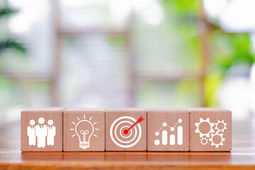 Wooden blocks with business icons showing target, representing business strategy, goal setting,...