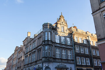 Obraz premium Old building stands tall on a busy city street, showing detailed architecture and blue sky above. Colorful buildings line the street in a historic district in Gdansk, Poland
