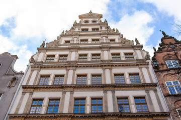 Tall building stands in the city with detailed design seen from below. Clear sky adds to the scene of urban life. A cobblestone street in Gdansk, Poland