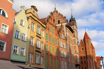 Several historical buildings stand closely together in Gdansk. The sky is clear, and the light is warm in the afternoon.