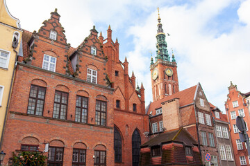 Fototapeta premium Brick buildings stand in Gdansk with a clock tower of Town Hall visible in the background under a blue sky. Poland