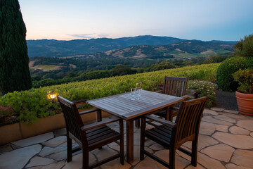 An inviting outdoor dining area set for two, featuring wooden furniture and a breathtaking view of rolling hills, perfect for enjoying a fine meal in a tranquil environment.