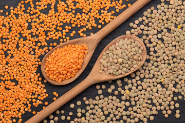 Wooden spoons with red and green lentils on black backround, top view