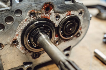 Disassembled old car gearbox with gears and tools on a workbench in an auto service garage. Repair, maintenance, and replacement of worn mechanical transmission parts in a vehicle.