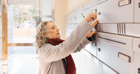 Senior woman opening communal mailbox checking for mail