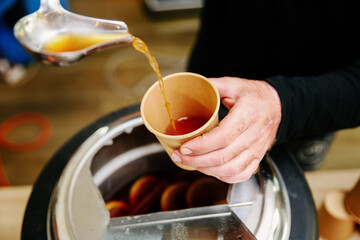 Close-up Action Shot of a Person Pouring Sangria or Iced Beverage from a Stainless Steel Ladle into a Disposable Brown Kraft Paper Cup at an Outdoor Event or Summer Bar