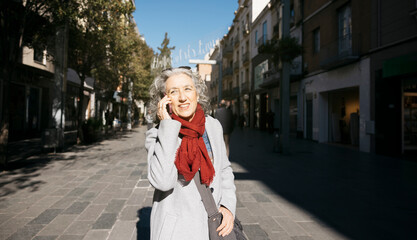 Senior woman talking on phone walking urban street
