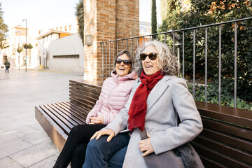Senior women friends laughing on urban park bench
