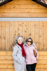 Senior women friends smiling hugging standing against wooden wall