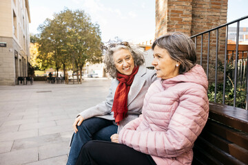 Senior women friends enjoying casual conversation on city bench