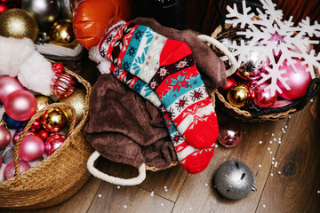 Festive Christmas Decor: Patterned Red, White, and Blue Woolen Socks and a Brown Blanket Tucked into Woven Baskets Filled with Ornaments, Alongside a White Snowflake Accent on a Dark Wood Floor
