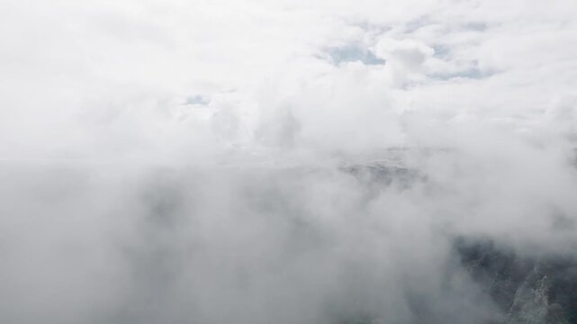 An aerial view of the mountains on a sunny summer day. Flying through thin clouds. Epic mountain views from a bird's eye view.