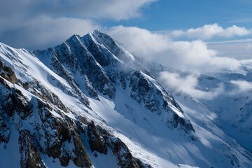 Fototapeta premium A stunning view of a rugged snow-capped mountain range being gently touched by clouds, portraying the beauty and power of nature's breathtaking landscapes.
