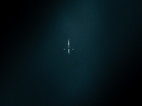 Aerial view of a lone scull slicing through the inky waters of the Charles River, a serene beacon of light in the darkness, Boston, Massachusetts, United States.