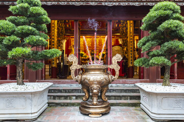The bronze incense burner with burning joss sticks in front of a richly decorated altar inside Hanoi's Temple of Literature
