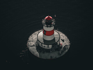 Aerial view of a vibrant red and white lighthouse standing proudly on a circular platform amidst the dark, tranquil sea, Fall River, Massachusetts, United States.