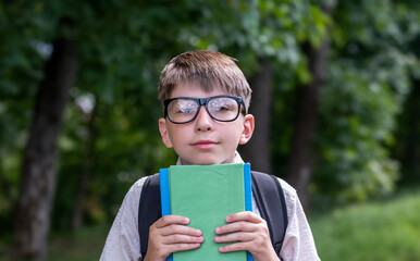 Education Concept Portrait of happy primery school child boy looking at camera, holding stack of academic books and wearing backpack banner. Back to school. Funny face in glasses screeming from enjoy.
