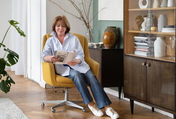 Elegant grandmother sitting at home reading a magazine