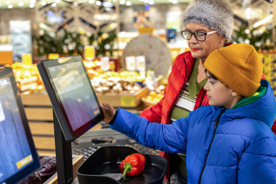 Young Boy Assisting His Grandmother With Digital Self Service Technology During Grocery Shopping. family support, tech literacy, active aging, and everyday grocery shopping