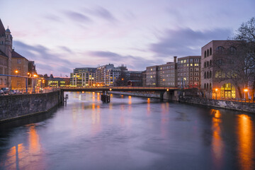 View of a tranquil river reflecting the city's golden lights under a dusky sky, highlighting the architectural elegance of buildings, Berlin, Berlin, Germany.