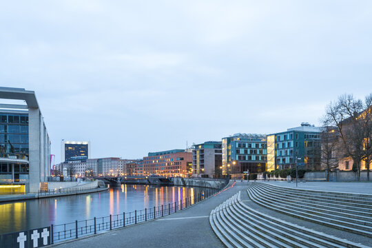 View of the tranquil Spree River reflecting the soft glow of city lights along modern parliament buildings and concrete steps, Berlin, Berlin, Germany.