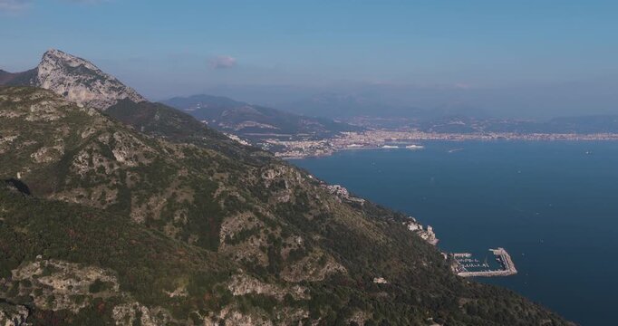 Aerial view of a rugged mountain range meeting the azure sea, alongside a small port nestled at the base, Erchie, Amalfi Coast, Italy.