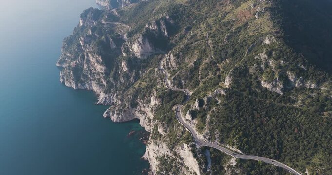 Aerial view of a winding road hugging the rugged coastline, contrasting with the deep blue sea and lush green cliffs, Erchie, Amalfi Coast, Italy.