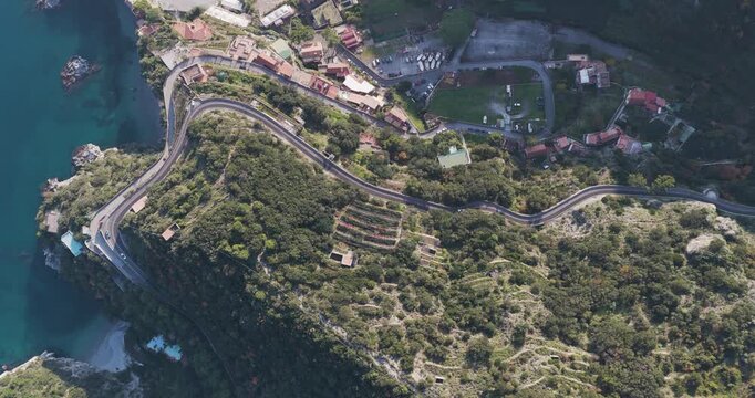 Aerial view of the winding road hugging the rugged coastline, contrasting with the turquoise sea and lush green vegetation, Erchie, Amalfi Coast, Italy.