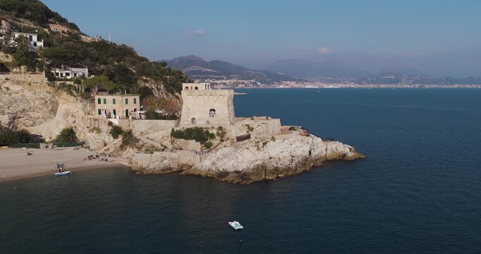 Aerial view of Torre La Cerniola, a historic tower on a rocky outcrop surrounded by deep blue sea contrasting with the light buildings, Erchie, Amalfi Coast, Italy.