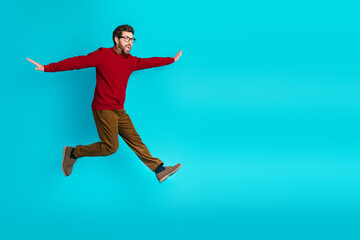 Fototapeta premium Young man in red sweater leaps with outstretched arms against blue background energy joy and lifestyle for advertising fashion and lifestyle projects