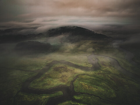 Aerial view of the marshland's winding waterways, veiled in ethereal mist beneath a somber sky, a serene yet dramatic landscape unfolds, Gloucester, Massachusetts, United States.