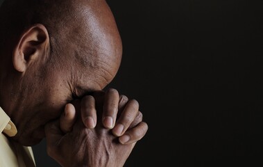 Naklejka premium man praying to god with hands together portrait view of Caribbean man praying with black background with people stock photo stock image