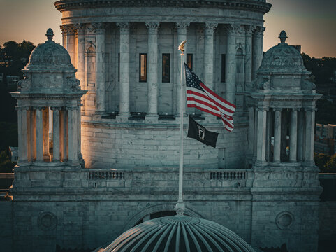 Aerial view of the Rhode Island State House bathed in the warm glow of sunset, flags fluttering proudly against the classical architecture, Providence, Rhode Island, United States.