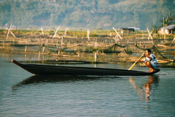 Lake Sebu, Philippines - 29 May 2015: View of a lone figure gliding across the tranquil lake in a slender boat, the calm waters reflecting the distant hills.