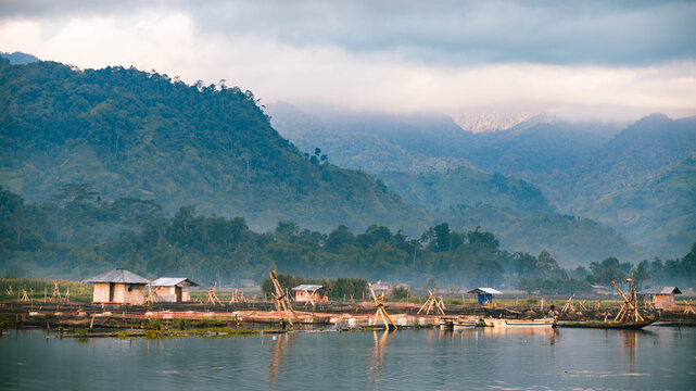 View of stilt houses standing serenely on the tranquil water, reflecting the misty mountains and lush greenery in Lake Sebu, Soccskargen, Philippines.