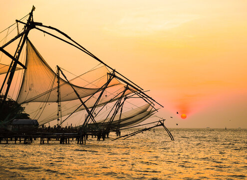 View of Chinese fishing nets silhouetted against a radiant sunset, casting golden hues across the tranquil waters, a timeless scene, Kochi, Kerala, India.